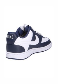 Sneaker Nike con una toma superiore in pelle bianca con accenti blu navy, allacciatura frontale, collo imbottito e suola in gomma testurizzata.