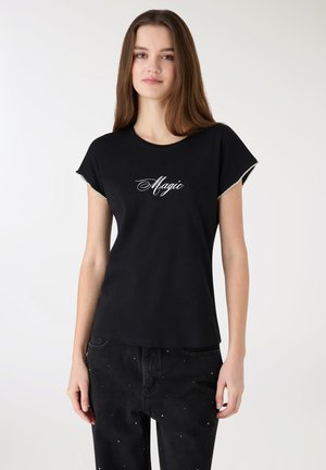 Czarna bawełniana koszulka z krótkimi rękawami, z napisem „Magic” w białym, kursywnym stylu. Koszulka ma zaokrąglony dekolt i luźny krój.