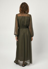 Lange, transparante olivegroene jurk met geplooide buste, elastische taille en wijd uitlopende mouwen. Glad materiaal en enkelgrote zoom.