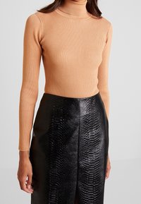 Col roulé côtelé en beige chaud, silhouette ajustée. Associé à une jupe midi en similicuir noir avec texture imprimé serpent et fente latérale.