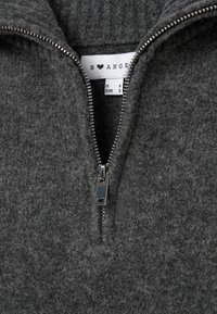 Sudadera de forro polar gris oscuro con cremallera de medio largo, que presenta un tirador de cremallera de metal plateado y cuello acanalado. Las etiquetas de cuidado son visibles.