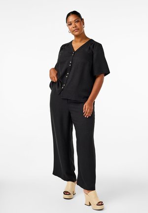 Top corto negro de manga corta con escote en V y detalles de botones, combinado con pantalones negros de pierna ancha. Sandalias de cuña en color crema. Textura suave.