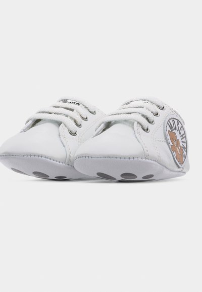 Λευκά βρεφικά παπουτσάκια με μικρές μαύρες κουκκίδες στις σόλες, λευκά κορδόνια και πλαϊνό ύφασμα με αρκουδάκι και την επιγραφή "Moschino".