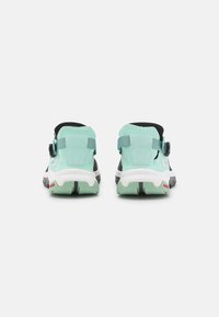 Vista trasera de zapatillas deportivas con un diseño en verde menta y negro, tejido texturizado, correas ajustables y una suela blanca de contraste.