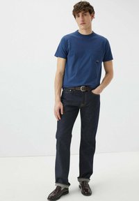 T-shirt in cotone blu navy con taschino, abbinato a jeans denim scuri. Il modello indossa una cintura in pelle marrone e scarpe nere.
