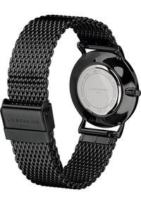 Svart klocka i rostfritt stål med ett vävt mesharmband, rund urtavla och spänne. Har en polerad baksida med varumärkesdetaljer.