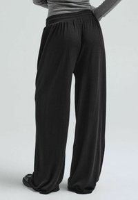 Schwarze, weit geschnittene Hosen mit weicher Textur und elastischem Bund, die eine lockere Passform und ein gerafftes Design aufweisen. Schlicht und vielseitig einsetzbar.