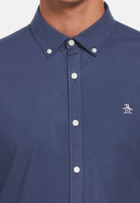 Navy blue button-up shirt in textured fabric, featuring a point collar, white buttons, and a small embroidered penguin logo on the chest.