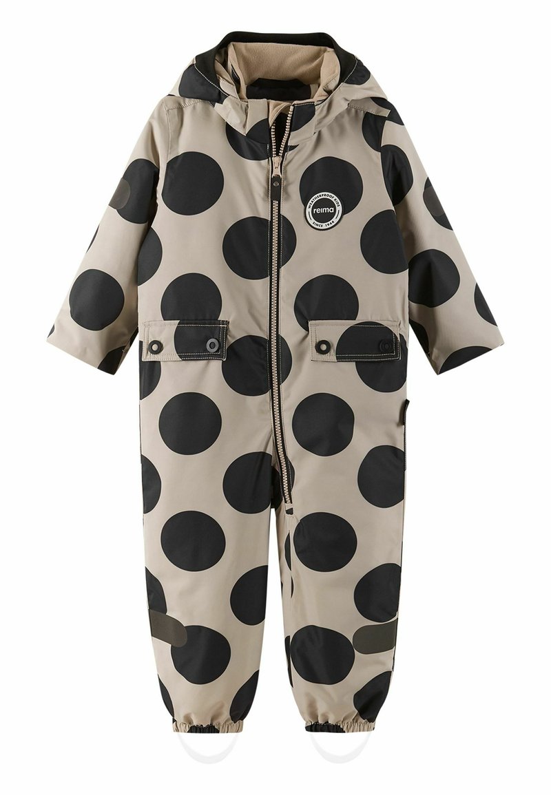 Béžový dětský dešťový oblek s velkými černými puntíky, přední zip, dvě náprsní kapsy, elastické manžety a kapuce. Odolný, voděodolný materiál.