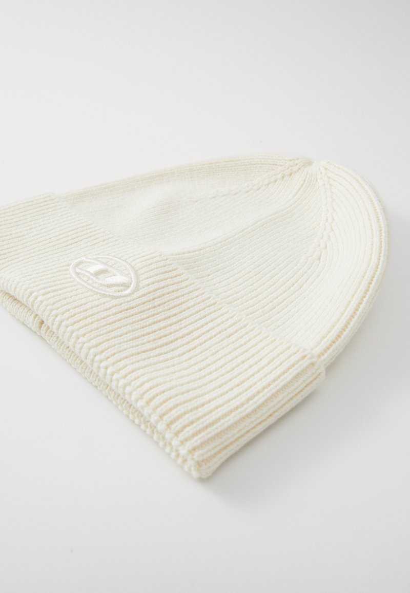 Bonnet en tricot couleur crème avec une texture côtelée et un revers replié, présentant un petit logo brodé à l'avant.