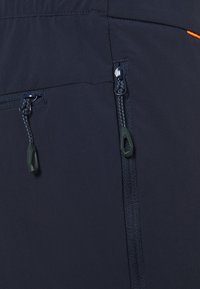 Tela azul marino con un bolsillo con cremallera y tiradores. La textura es suave y hay un acento naranja cerca de la costura. Diseño duradero.