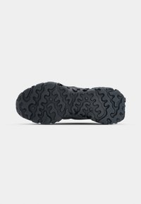 Semelle de chaussure en caoutchouc noire avec des motifs ondulés et circulaires profonds pour une bonne adhérence sur une surface plane.