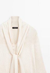 Top avvolgente beige con una texture morbida e arricciata, caratterizzato da un profondo scollo a V e un dettaglio frontale attorcigliato. Etichetta che dice "Massimo Dutti."