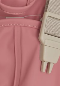 Rosa ryggsäck gjord av glatt material med en strukturerad kropp, sömnadsdetaljer och ett beige justerbart remspänne.