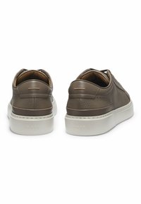 Un paio di sneaker in pelle marrone con suole bianche, viste da dietro, impreziosite da un discreto logo "BOSS" impresso sul tallone.
