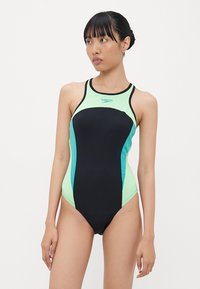 Maillot de bain noir avec des accents vert menthe, doté d'un dos nageur et de panneaux latéraux dans une couleur contrastante. Fabriqué en matériau extensible.
