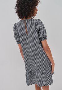 Svart och vit rutigt klänning med puffärmar, en nyckelhålsöppning bak och en volang i nederkanten. Tillverkad av bomullstyg.