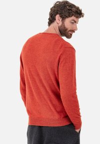 Pull orange en maille avec un col rond et des poignets côtelés. Présente une finition texturée et une silhouette ajustée. Vue de dos.