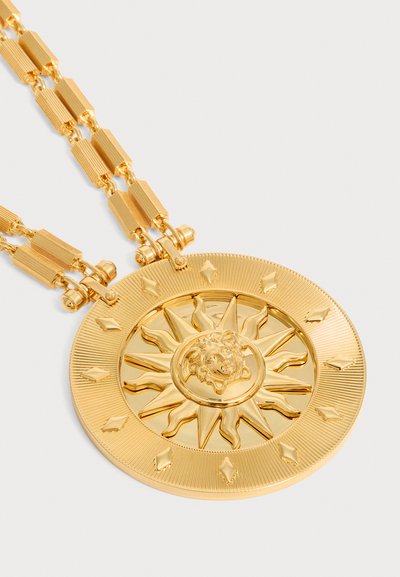 Collier en or avec un grand pendentif rond représentant un soleil avec une tête de lion au centre et des détails en forme de losange sur le bord extérieur.