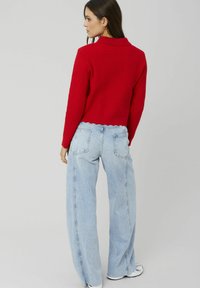 Pull court rouge côtelé avec un col à revers, associé à un jean large taille haute bleu clair et des baskets blanches.