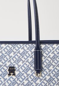 Borsa a tracolla blu navy e bianca con motivo geometrico, manici in pelle, cuciture a contrasto e un'emblema dorato sul davanti.