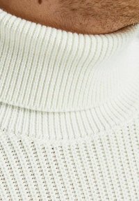 Weißer gerippter Rollkragenpullover mit strukturiertem Muster. Der Kragen bietet eine hohe, enge Passform, die das Strickdesign und die Webart betont.
