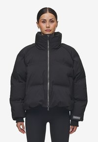 Svart puffjacka med hög krage, framfickor med dragkedja och ribbade mudd. Tjock, vadderad design med en logotyppatch på ärmen.