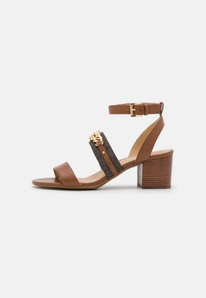 Brun sandal med blokhælhæl i læder, ankelrem, mørk stofrem med guldkædedetalje og åben tådesign.