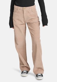 Beige corduroy broek met een recht model, voorzien van voordewpockets en een gouden knoop. Gecombineerd met een zwart geribd langemouwtop en sneakers.