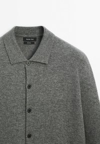Cardigan en laine grise avec boutons, col rabattable et boutons noirs, étiquette Massimo Dutti.