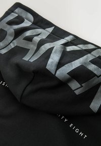 Fekete kapucnis pulóver nagy, fényvisszaverő ezüst "BAKER" felirattal a kapucnin. Egyszerű dizájn, puha textúrával és diszkrét márkajelzéssel alul.