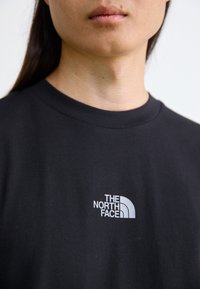 Svart bomull t-skjorte med hvit logo av "THE NORTH FACE" på venstre bryst, rund hals og jevn tekstur.