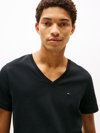 Maglietta di cotone nera con scollo a V. Presenta maniche corte e una piccola etichetta logo sul petto sinistro. Texture liscia.