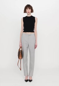Haut sans manches noir, pantalon gris ajusté, et escarpins noirs à bout pointu. Porte un sac à main en cuir marron avec des accents foncés.