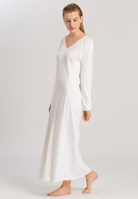Lungo vestito bianco realizzato in tessuto morbido, con scollo a V, maniche lunghe e una silhouette fluida che arriva fino a terra.