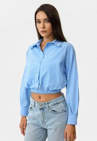 Lichtblauw cropped button-up shirt met lange mouwen en een geplooide zoom, gecombineerd met hooggemaakte lichtblauwe jeans. Glad textiel met een fijne structuur.
