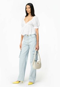 Top bianco con maniche a sbuffo e scollatura a V profonda, abbinato a pantaloni cargo azzurri chiari. Gli accessori includono una borsa bianca e scarpe col tacco gialle.