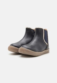 Botas de tornozelo em couro preto com um acabamento suave, laterais elásticas e uma borda recortada, montadas sobre uma sola de borracha castanha clara.
