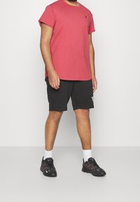 T-shirt en coton rouge à manches courtes et encolure ronde, associé à un short noir avec un logo imprimé. Chaussures de sport noires avec des accents rouges.