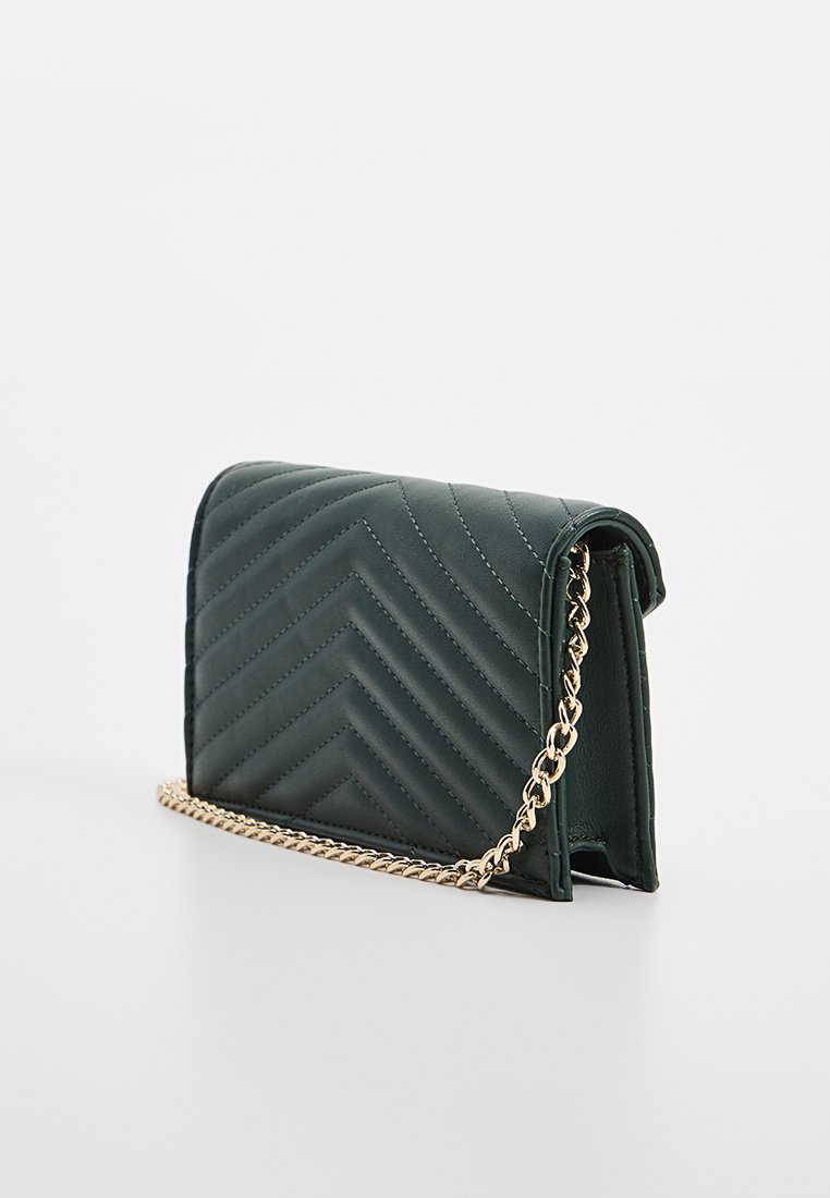 Sac à main en simili cuir vert matelassé avec une bandoulière en chaîne dorée, affichant un motif en zigzag et une forme structurée. Design compact.