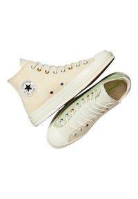Tenisii Converse cu gât înalt și joasă au un superior din pânză bej cu un finisaj texturat, accente verde deschis și tălpi din cauciuc alb.