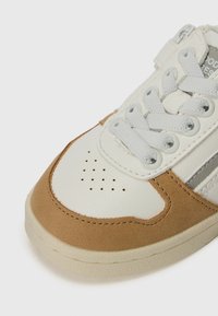 Läder sneakers med vit tå, tan mocka detaljer, grå ränder och strukturerad gummisula. Snörningen är ljusgrå med perforerade detaljer.