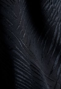 Schwarzer Textilstoff mit einer Zickzackmusterung, hergestellt aus gewebtem Material mit subtiler glänzender Oberfläche und unterschiedlichen Garnstärken.