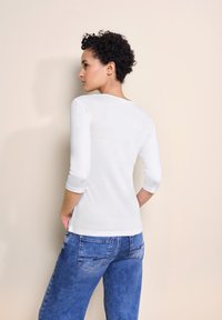 Hvid langærmet top i et tætsiddende design, parret med lyseblå denimjeans. Enkel, glat tekstur med rund halsudskæring.