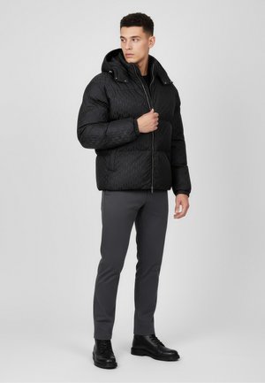 Black puffer jacket with a quilted pattern, hood, and front zipper, paired with dark gray slim-fit pants and black lace-up boots.