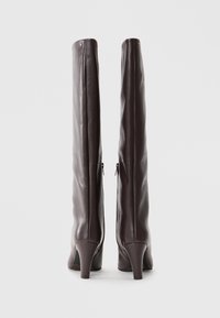 Stivali alti al ginocchio in pelle marrone con una texture liscia, silhouette snella e tacchi affusolati. Presentano una chiusura con zip su ciascun lato.