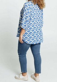 Blusa blu e bianca con motivo, con maniche larghe, abbinata a pantaloni in denim aderenti e sneakers bianche. Tessuto dalla superficie liscia, design casual.
