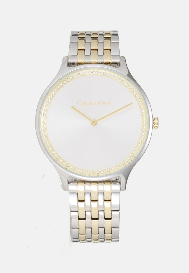 Reloj en tonos plateado y dorado con caja redonda de acero inoxidable, bisel de cristal, esfera blanca minimalista y pulsera de metal vinculada.