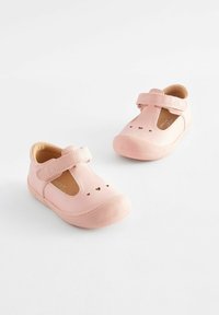 Rosa Lederschuhe mit einem Klettverschluss, abgerundeter Spitze und kleinen Herz-Ausschnitten im oberen Bereich. Weiche Sohle für mehr Komfort.