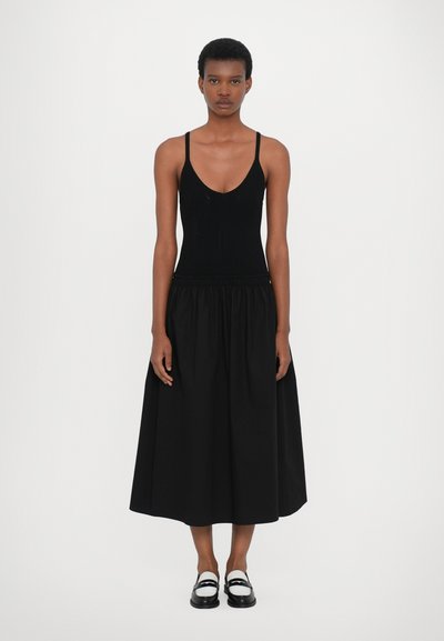 Zwarte gebreide bodysuit met diepe V-hals, gecombineerd met een maxi-rok in zwart met een elastische tailleband en een soepele textuur.